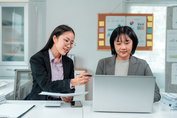 Two asian businesswomen are having a meeting in the office, analyzing financial data using a laptop and documents