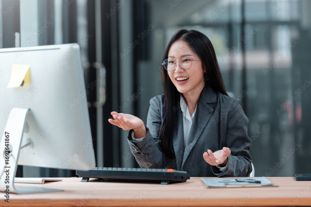 Poster smiling businesswoman gesturing while having a video conference with desktop computer in modern offi