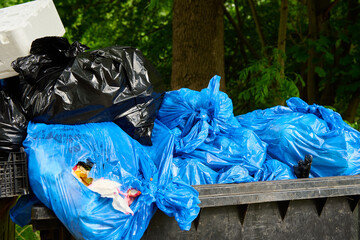 Black and blue plastic garbage bags in large dumpster. Full outdoor garbage container