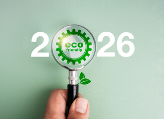Magnifying glass focusing on eco-friendly gear icon between numbers 2026 on green background, symbolizing green goals, sustainable future, and environmental responsibility for the new year 2026.