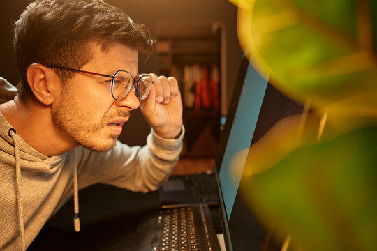 Man in glasses leaning forward and squinting at computer screen. Concept of eye strain, poor vision, digital fatigue and overwork