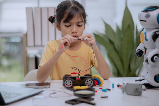 Asian girl focused on building a robot car using wires, gears, and tools at home, concept of STEM education, robotics workshop, DIY engineering, and creative technology learning for kids.