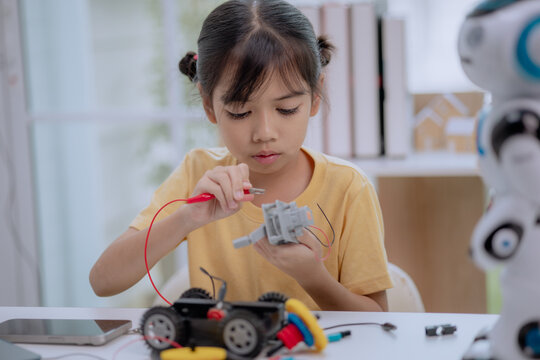 Asian girl focused on connecting wires to robot motor at home, concept of STEM education, DIY robotics, maker space, hands-on engineering, and creative technology learning activities for children.