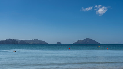 Beautiful seascape. A calm turquoise ocean, silhouettes of people in the water, orange buoys, a boat in the distance. Mountains on the horizon, against a blue sky, clouds. Philippines. Palawan
