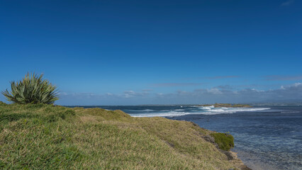 The waves of the turquoise ocean are raging and foaming between the islands. Green grass, yucca bushes on the coast. Clouds, blue sky. Copy space. Mauritius.  Île aux Fouquets.   Prison Island