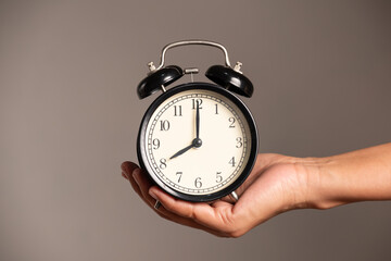 A man's hand holds an alarm clock in his hand.