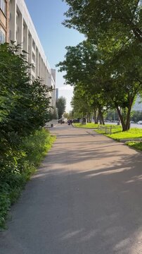 Amera moves smoothly along a long alley framed by trees and a modern building. An atmosphere of calm and serenity in an urban environment.