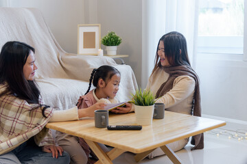 During a cozy winter day, a child reads a book with two adults near a window, the scene features a wooden table, mugs, and string lights creating a warm indoor atmosphere