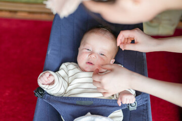 A baby is being held by a woman, who is touching the baby's face. The baby is wearing a striped shirt and he is looking at the woman. Concept of warmth and tenderness between the woman