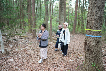 Fototapeta premium A group of people are walking through a forest, one of them holding a baby. Scene is peaceful and serene, as the group seems to be enjoying their time in nature