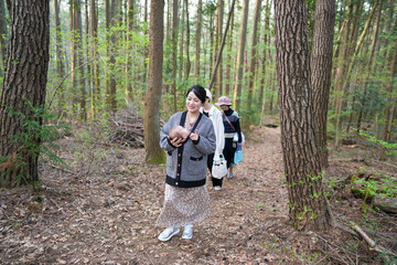 A woman is walking through a forest with a baby in her arms. The baby is wearing a hat