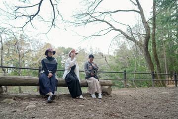 Three women sitting on a log in a park. One of them is wearing a hat. Scene is peaceful and relaxing