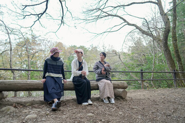 Three women sit on a log in a park. One of them is holding a baby. Scene is peaceful and relaxing