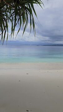 Relaxing on Tropical Beach with Calm Sea. 4K footage of a tropical beach scene with calm turquoise sea, white sandy shore, and feet resting on the beach, creating a peaceful holiday atmosphere.