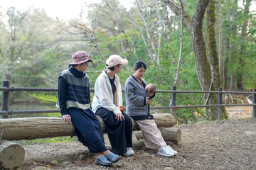 Three people are sitting on a log in a forest. One of them is holding a baby