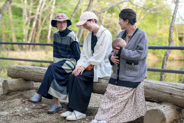Three women sit on a log in a park, one of them holding a baby. Scene is peaceful and relaxing, as...