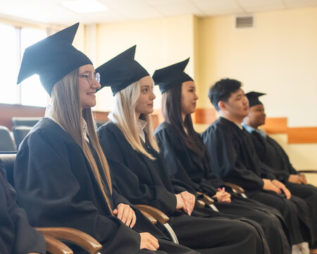 Young people in graduation gowns listen to a speech. 