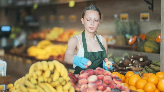 Working in supermarket - female salesman sorts through ripe flat peaches on the display case. High quality 4k footage