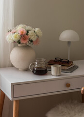 A bouquet of asters in a ceramic vase, coffee, a notebook, a laptop on a white table in the bedroom