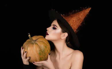 Halloween party. Halloween Witch posing with pumpkin in studio. Young woman in Halloween witch hat....