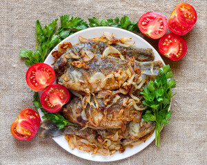 Fried fish with tomatoes and herbs. Plate with fried crucian carp