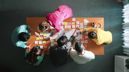Top down aerial view of skilled designer hold logo while discuss with team. Aerial business group working together sharing idea about logo graphic design by using sticky notes and tablet. Symposium. - Powered by Adobe