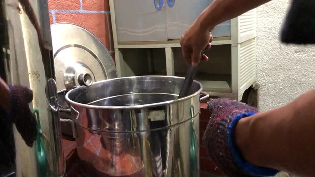 Asian man scalds a wine bottle in boiling water to pasteurize it, then places it on a wooden rack while  working in a small local winery.