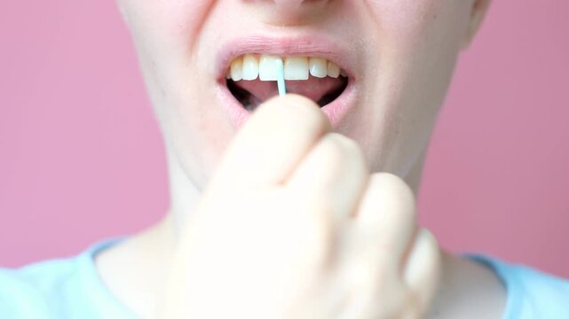 Young woman brushing teeth with disposable dental floss close-up on pink background