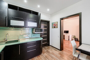 modern kitchen with dark wood cabinets, light green countertops, and an open doorway to a bright workspace