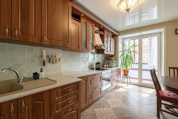 well-lit kitchen featuring wooden cabinets, tiled backsplash, light countertops, and patterned tile flooring.  A large plant sits near a window