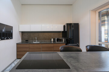modern kitchen featuring white cabinets, wood drawers, a black refrigerator, and a gray countertop with a black stovetop