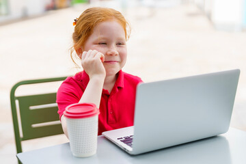 Young girl enjoys computer time at outdoor cafe while sipping on a warm drink during sunny afternoon