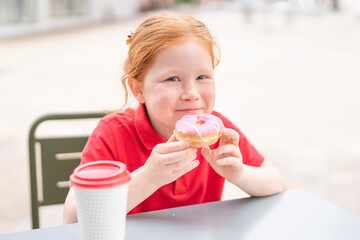 Child enjoys colorful donut and warm drink at outdoor cafe during sunny day in a bustling city
