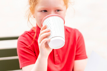 Young girl enjoying a warm beverage while sitting outdoors at a cafe during a sunny afternoon in a...