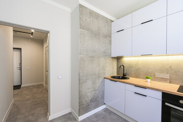 modern kitchen with white cabinets, a wooden countertop, and a black sink and faucet. A hallway is...