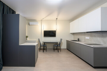 modern kitchen with gray cabinets, a dining table, and a TV on the wall. The room is well-lit