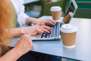 People typing on a laptop at an outdoor cafe table while enjoying coffee in the early afternoon sun...