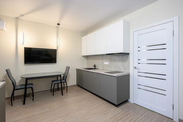 modern kitchen interior featuring gray and white cabinets, a dining table with chairs, and a...