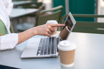 Person engaging with a laptop while sitting at an outdoor table during the day with coffee cups...