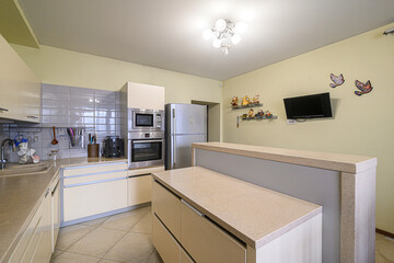 Modern kitchen with light yellow walls, beige cabinets, a tile backsplash, stainless steel...