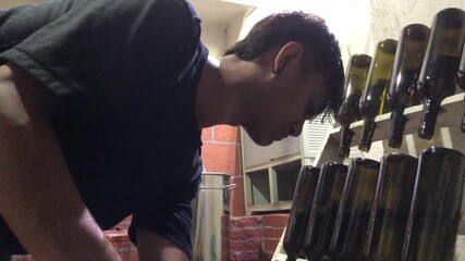 Asian man scalds a wine bottle in boiling water to pasteurize it, then places it on a wooden rack while  working in a small local winery. - Powered by Adobe