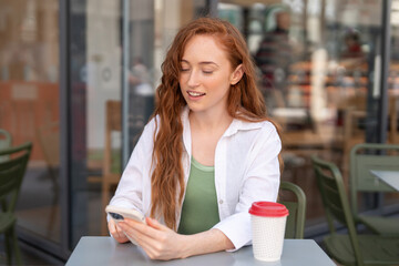 Young woman enjoying coffee while using smartphone at a modern cafe during daytime