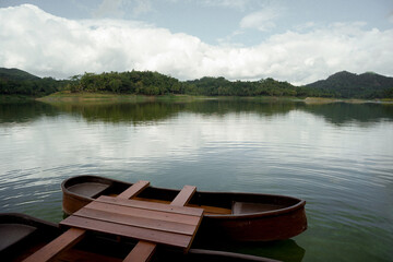 beautiful view of wooden boats on a lake with tree-lined hills under a cloudy blue sky