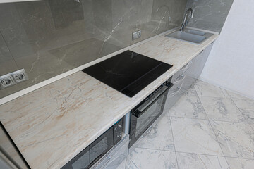 modern kitchen corner with marble-patterned countertop, a black induction cooktop, a stainless...