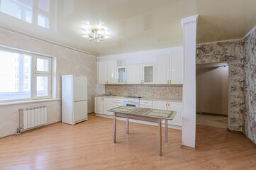 Bright kitchen with white cabinets, table, and large window. Light wood floors and textured walls. An open doorway leads to another room