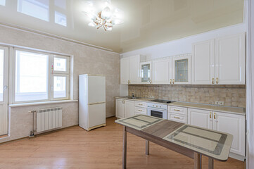 Bright kitchen with white cabinets, appliances, and a wooden floor. Natural light fills the room. A dining table sits in the foreground