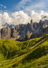 Naklejka premium Stunning vertical shot of Dolomites featuring dramatic rocky peaks, lush alpine meadows, clear blue sky. Classic mountain landscape of northern Italy, perfect for travel, outdoor themes.