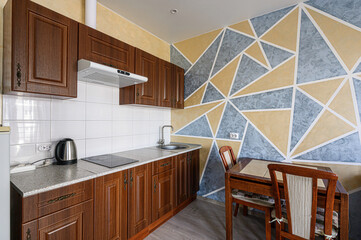 Cozy kitchen with wooden cabinets, tile backsplash, and a geometric accent wall in blue and gold. A dining table and chairs complete the scene