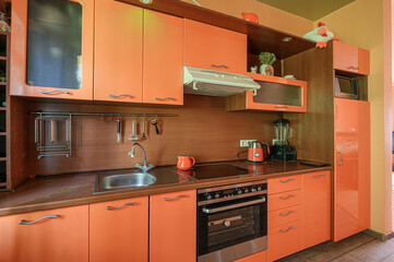 cozy kitchen with orange cabinets, brown countertops and backsplash. A stove and oven are visible,...