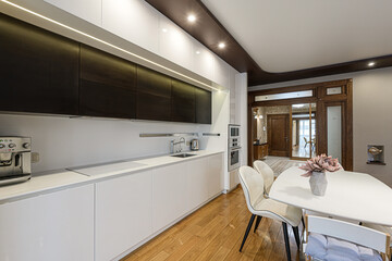 modern kitchen features sleek white cabinets, dark upper cabinets with strip lighting, and a dining area with a white table
